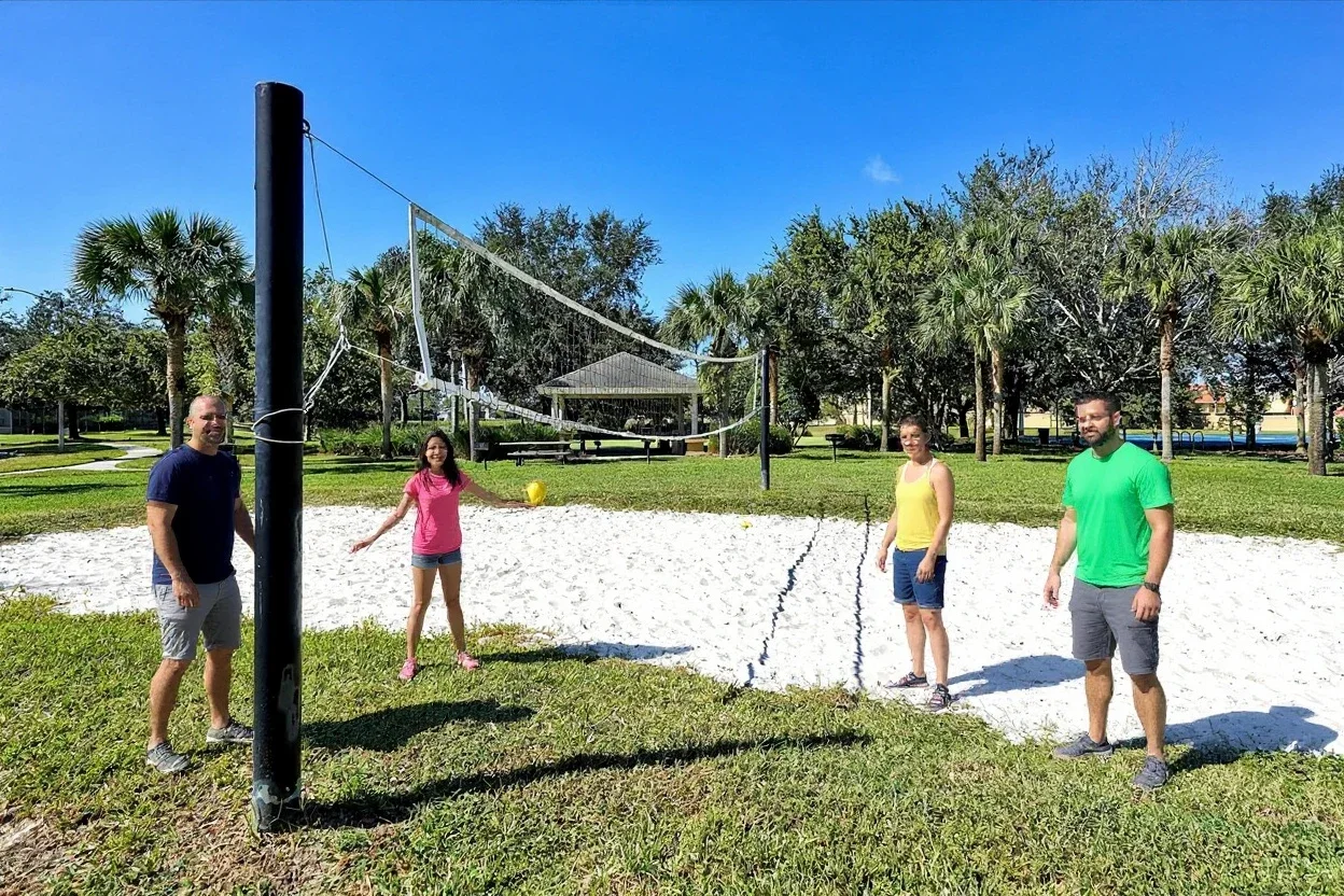 A family of six in plain t-shirts and shorts playing a casual game of sand volleyball, a dad jumping for the ball and kids laughing