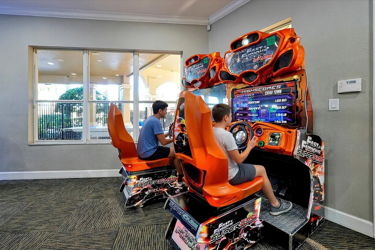 A teenage boy in a plain t-shirt playing the existing racing arcade game while his teenage sister cheers beside him