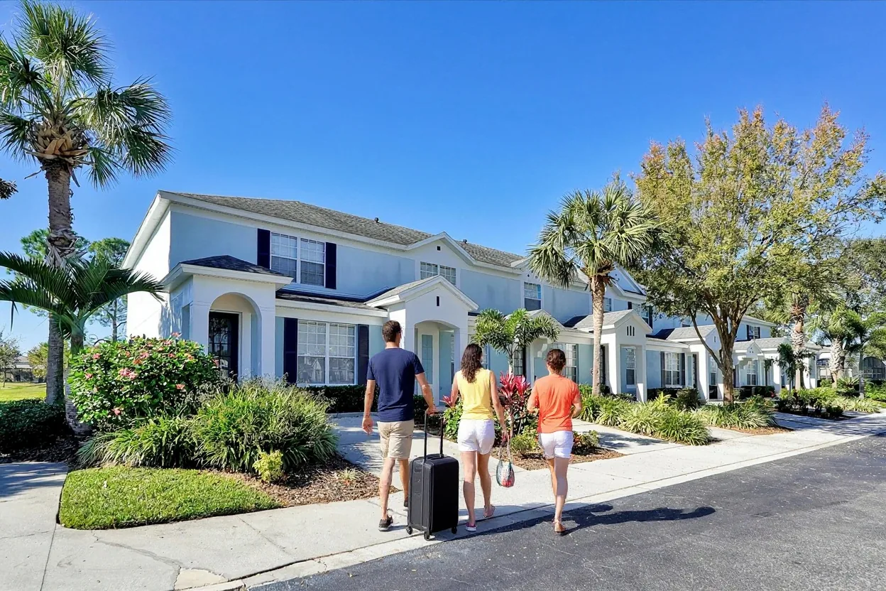 Guests rolling a suitcase along the sidewalk past Windsor Hills townhouses on a sunny day