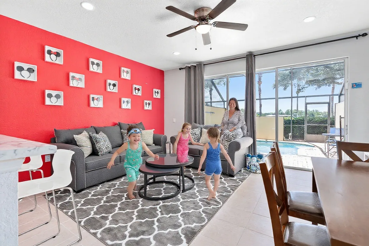 Two kids in swimsuits and goggles running happily toward the open sliding glass door to the pool, and an ordinary mom in a cover-up