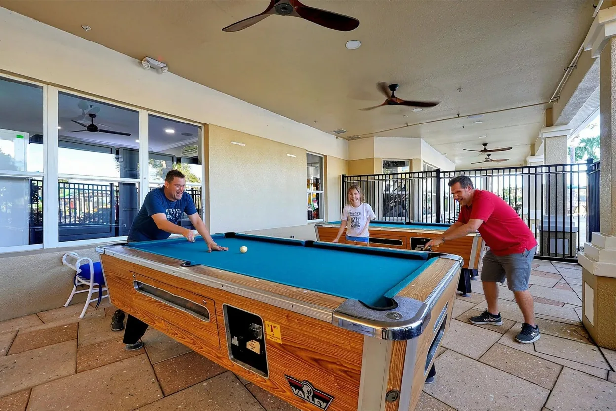 An ordinary dad and two kids playing pool at the existing billiards table, one kid lining up a shot, everyone laughing, in plain unprinted