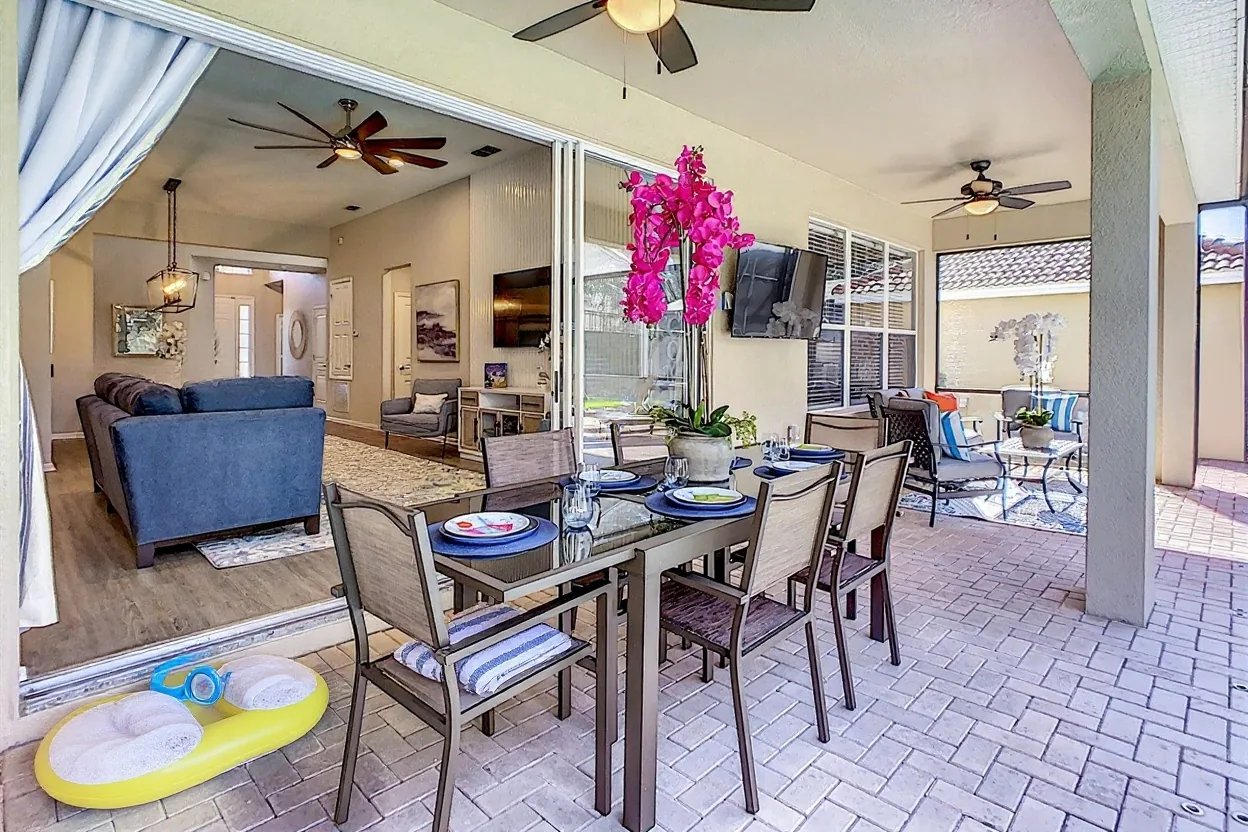 Rolled striped beach towels on two of the patio chairs, a plain bright pool float and kids' goggles by the open door, and a plain pitcher