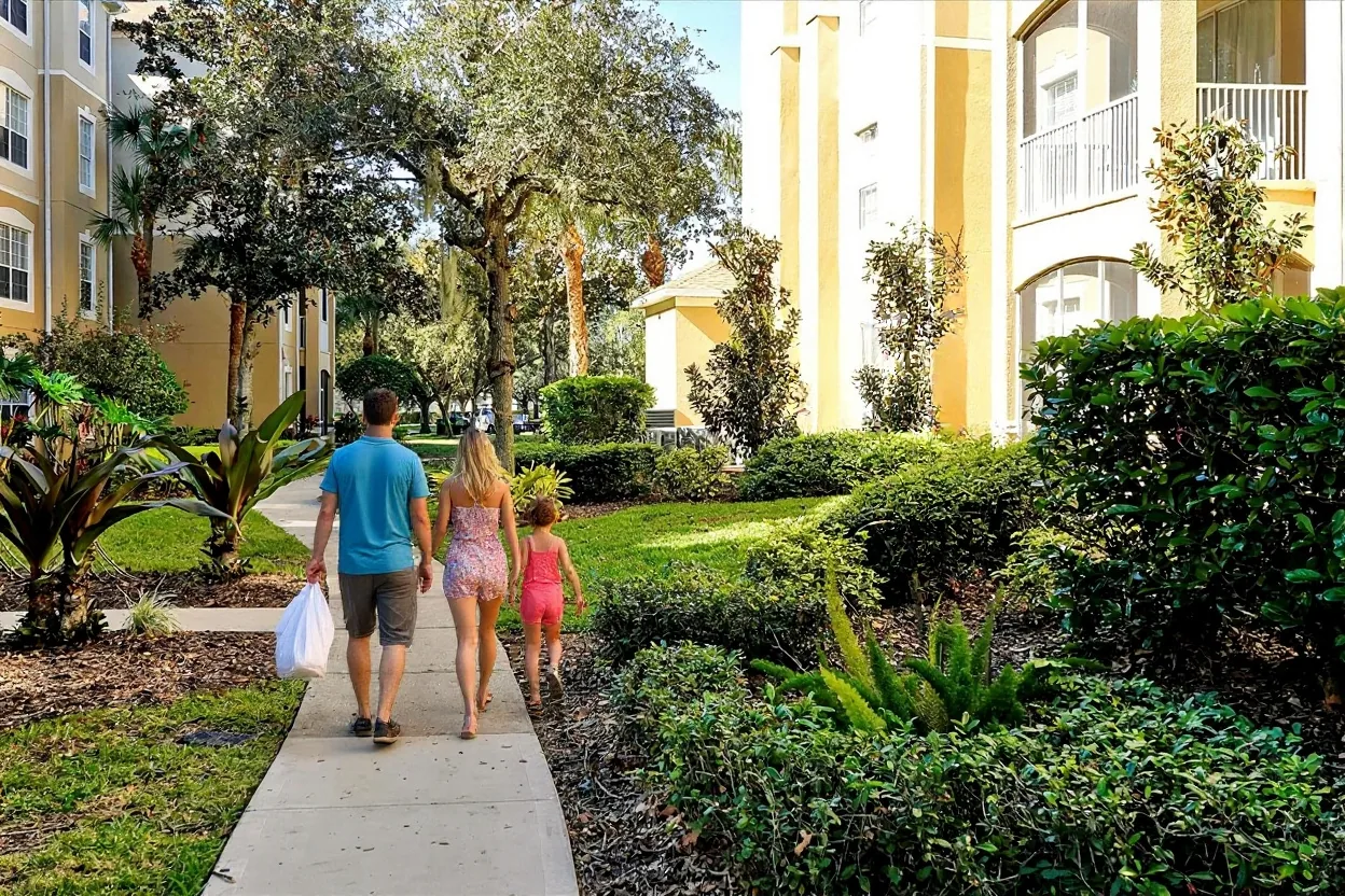 An ordinary family walking along the existing walkway toward the pool carrying a plain pool bag, towels and a pool noodle, kids skipping