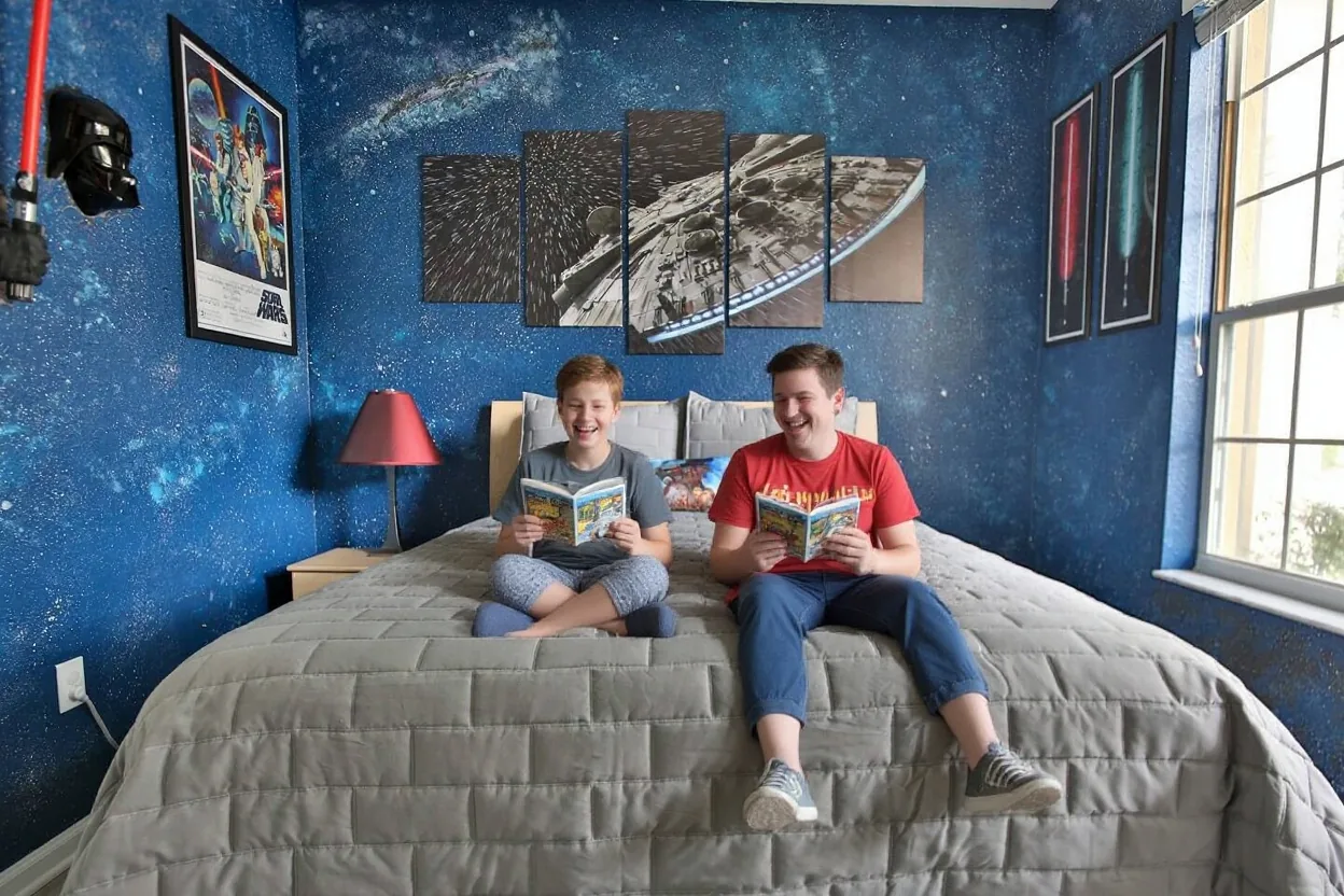 Two brothers in pajamas sitting on the existing bed reading comic books and laughing