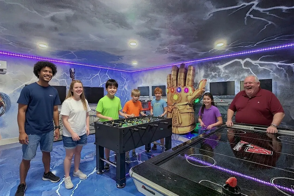 A group of cousins, four kids and two teens, playing the existing foosball table and air hockey table and cheering, with an ordinary uncle