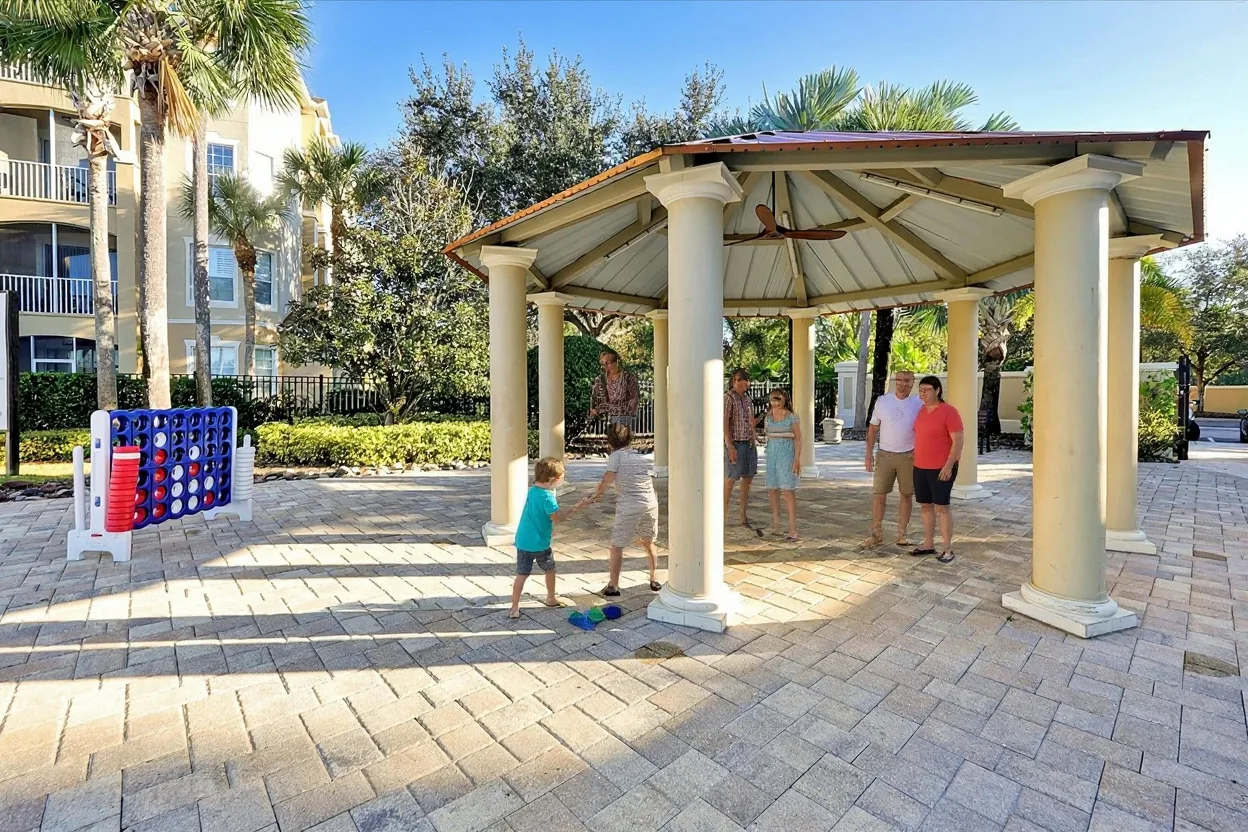 Two ordinary families on the existing paved stone patio around the gazebo: two kids playing the existing giant connect-four game and