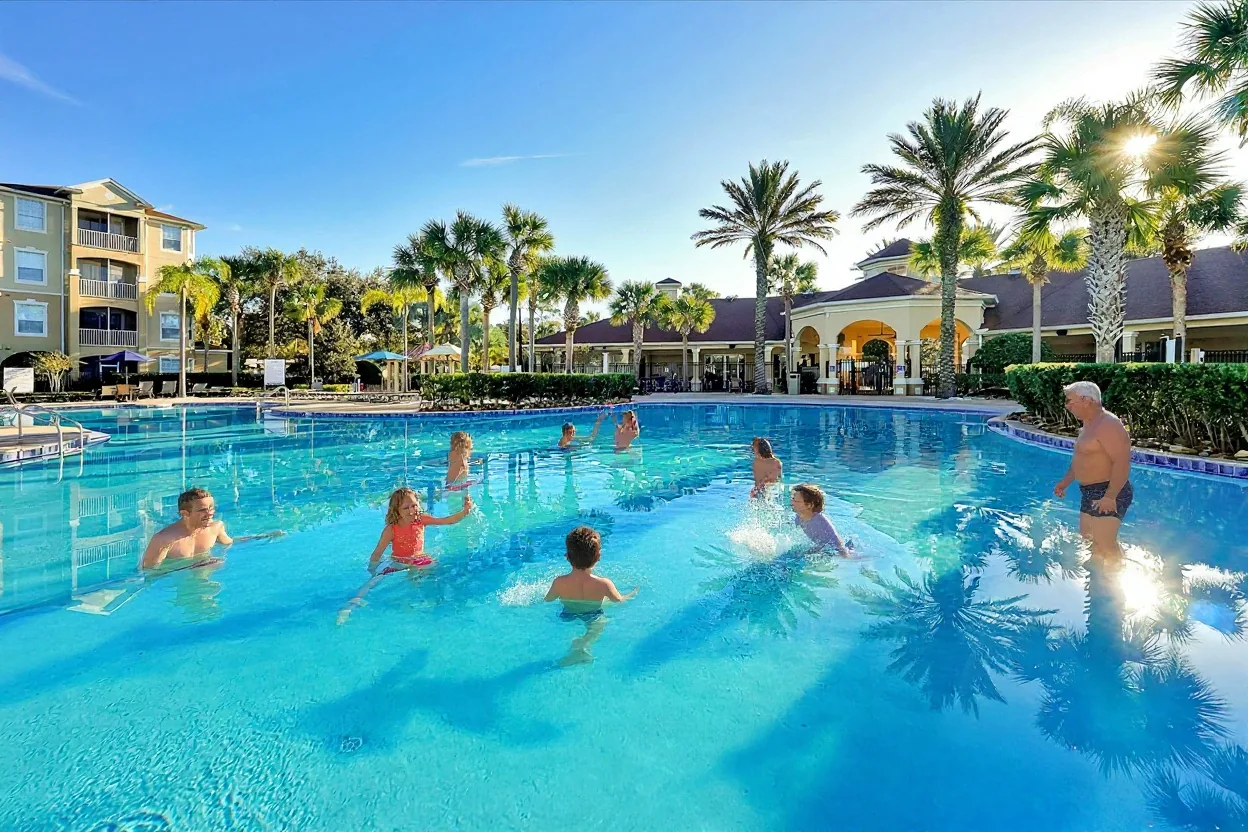 A few ordinary families enjoying the pool: kids splashing in the shallow area, a dad tossing a child gently in the water and a grandma
