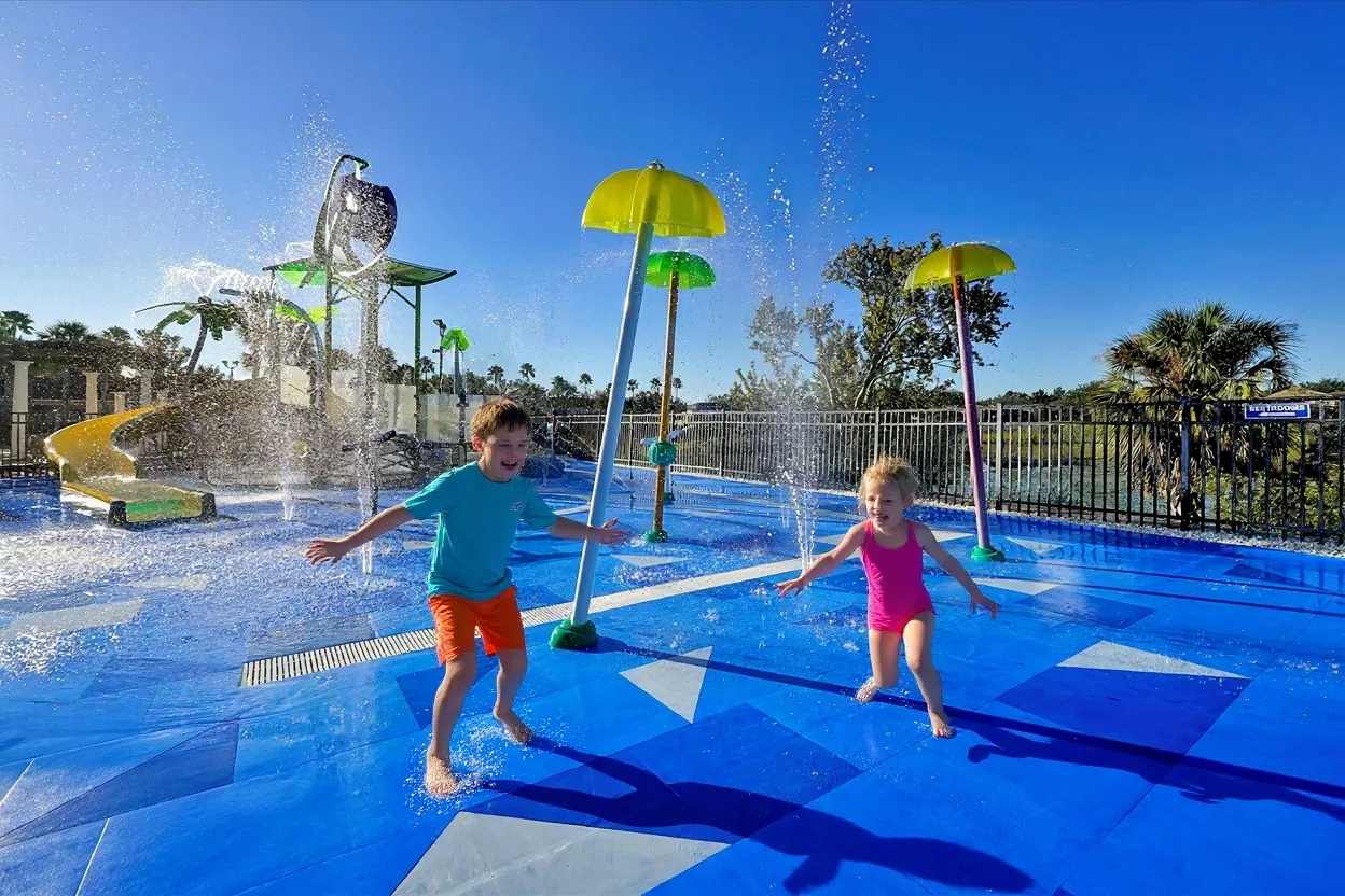 Two kids running and laughing through spraying water jets at the Windsor Hills Resort splash pad