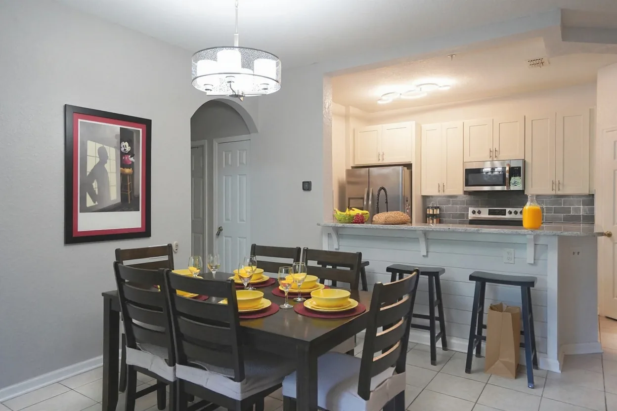 On the kitchen counters and the breakfast bar, clearly visible, place a big bowl of fresh fruit, a loaf of bread, a bunch of bananas, a jug of orange