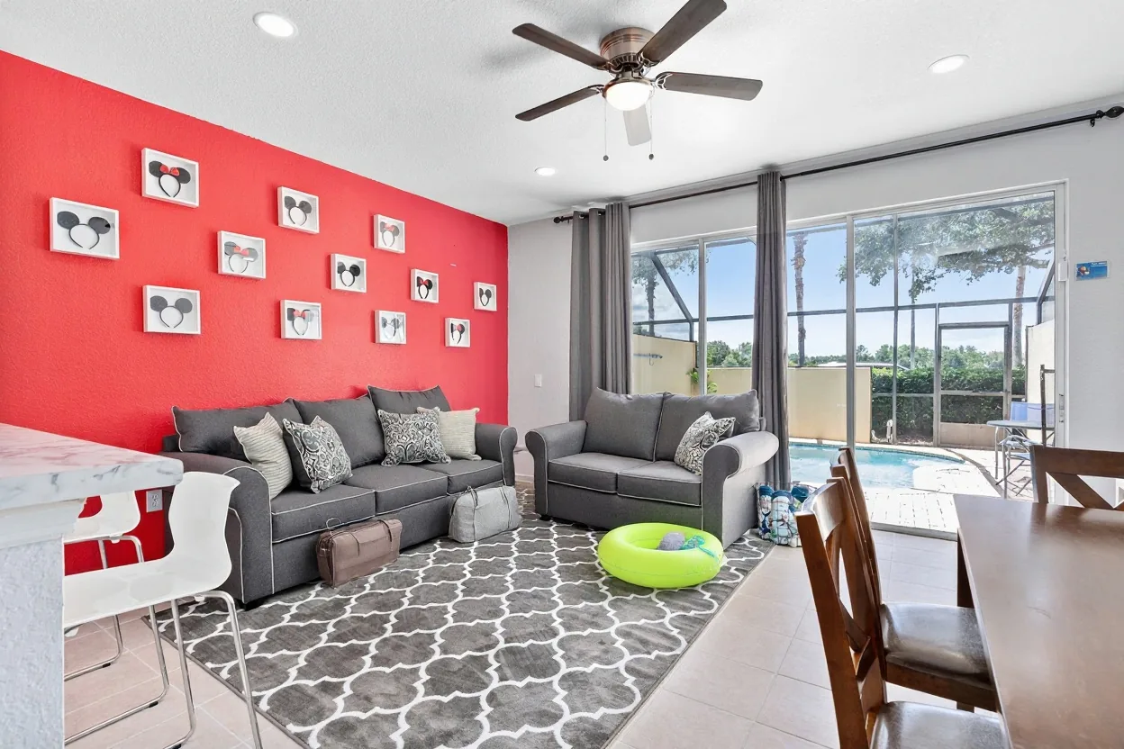 Two rolling suitcases and a plain duffel bag by the sofa, a plain pool bag with rolled towels and a bright pool float by the sliding door